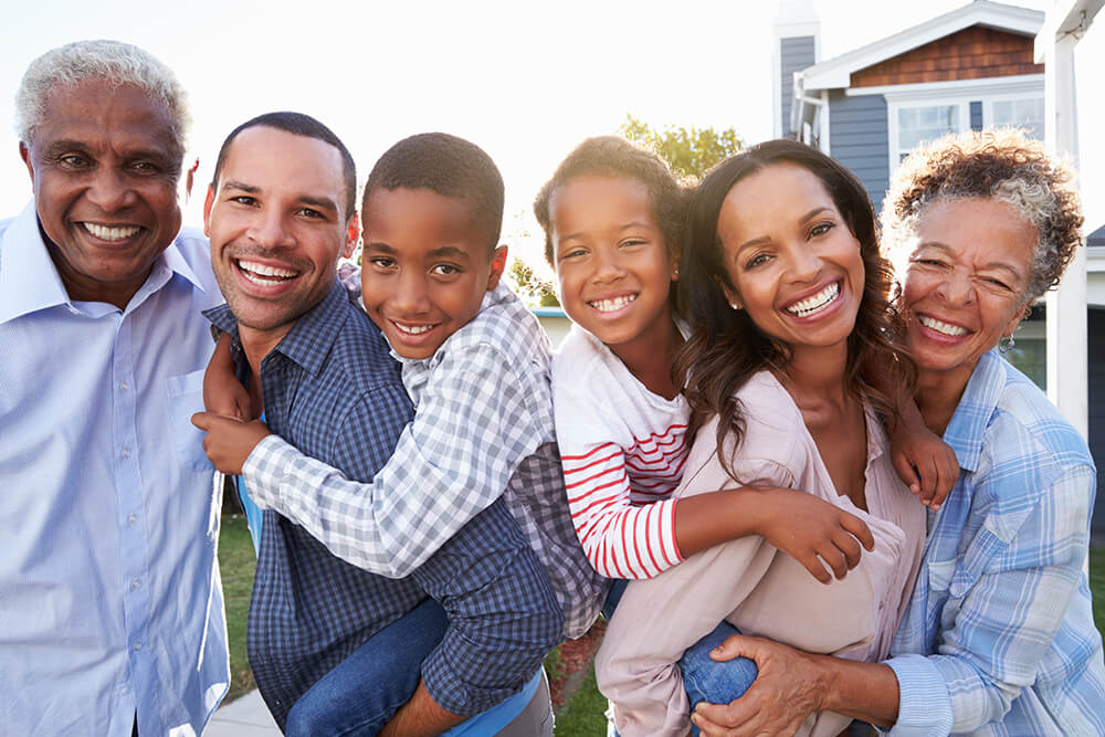 Adults and children smiling together outside a home.